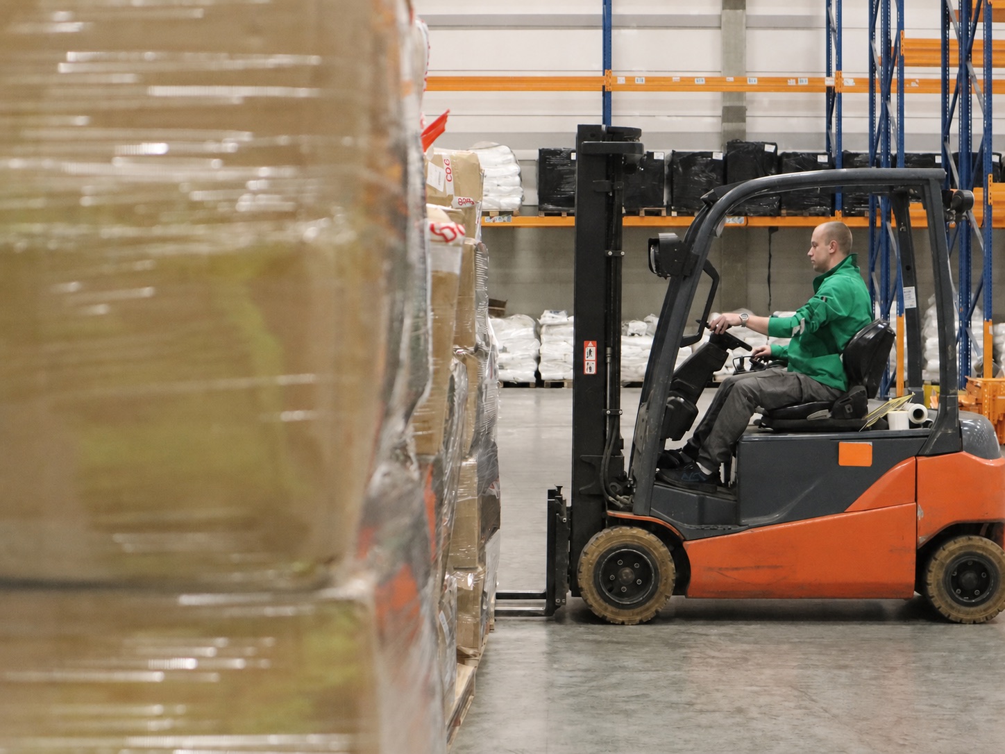 Warehouse forklift operator handling palletized goods without visible commercial branding.